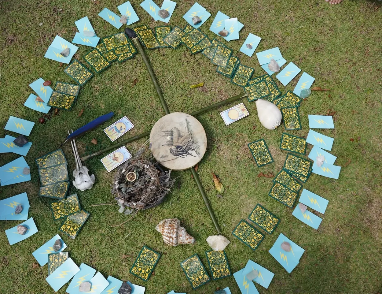 Altar com cartas, cristais, flores e tambor sobre a grama