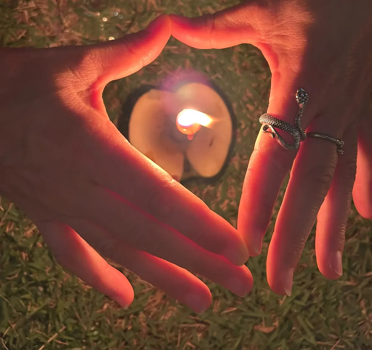 Mãos formando um coração em volta de uma vela acesa